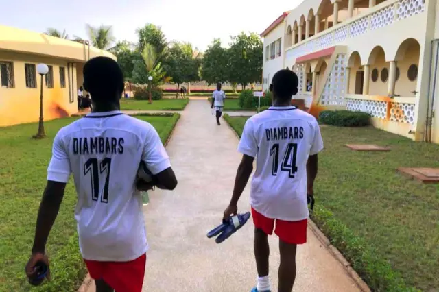 Deux joueurs vêtus de maillots blancs et de shorts rouges marchent en direction du terrain.